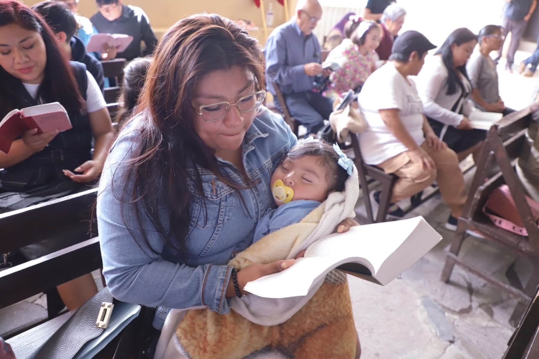 Tania holding her daughter as she reads her bible